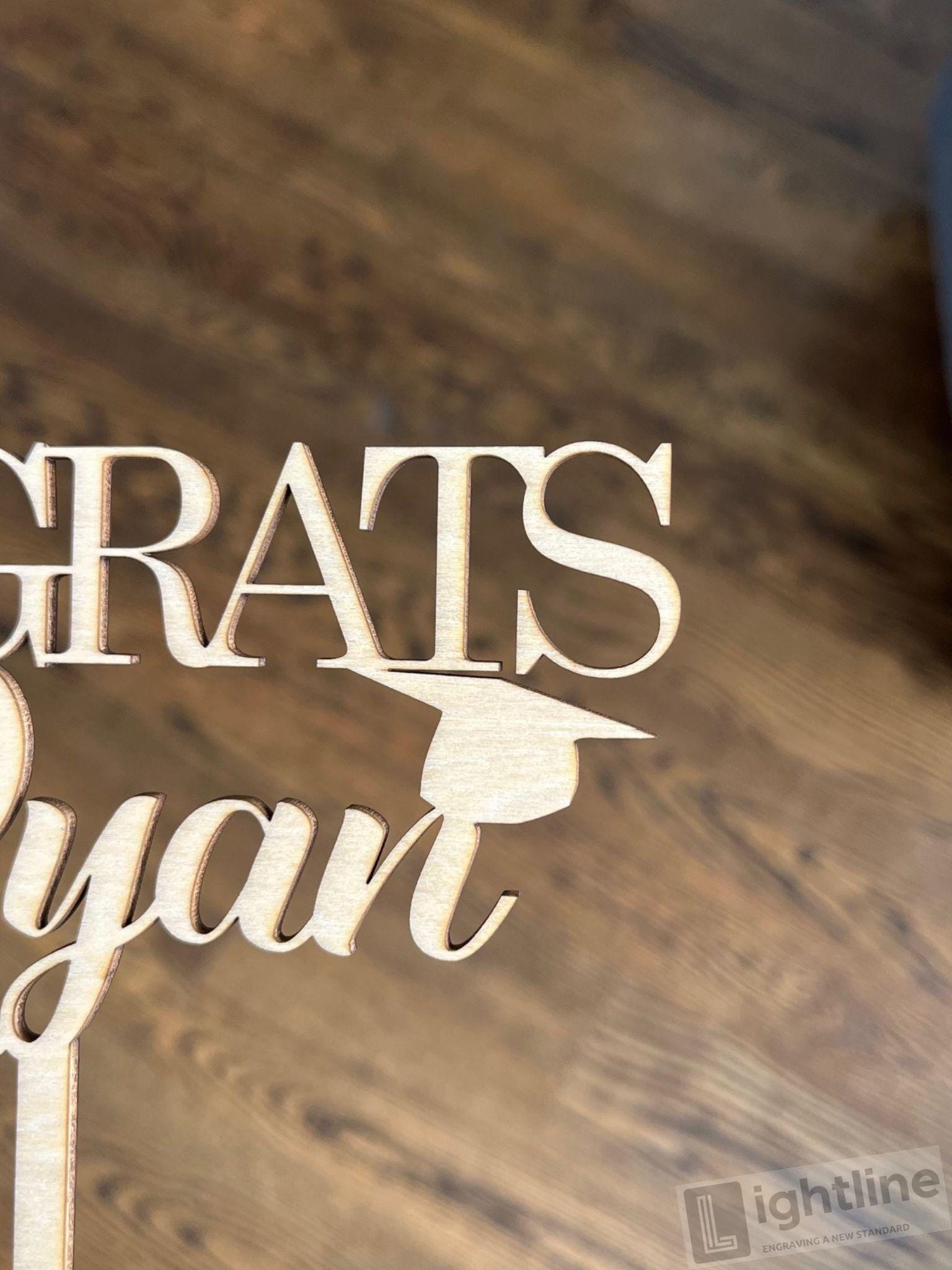 Wooden graduation-themed decorative sign with 'GRATS' and a graduation cap on a wooden surface.